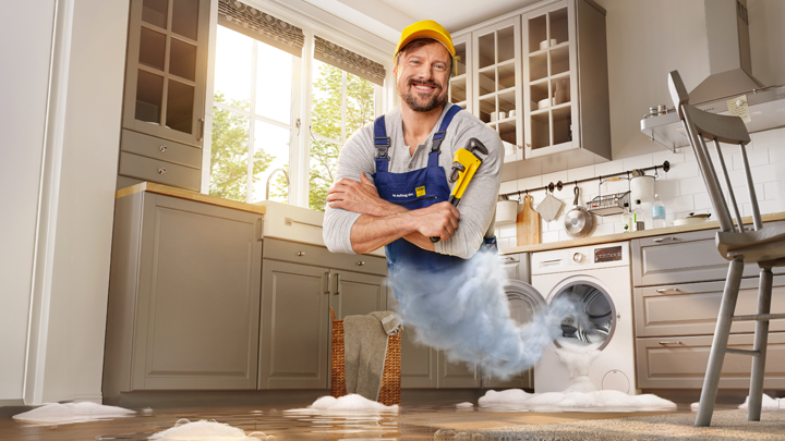 Handwerker mit Rohrzange erscheint aus auslaufender Wachmaschine 